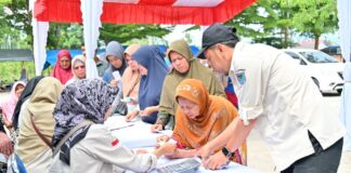 Petugas Pemko Payakumbuh melayani warga yang antre membeli kebutuhan pokok dalam Gerakan Pangan Murah di Pasar Padang Kaduduak.