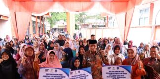 Sekelompok warga penerima Bantuan Langsung Tunai Sementara Kesejahteraan Rakyat (BLTS Kesra) 2025 di Payakumbuh berfoto bersama Wakil Wali Kota Payakumbuh saat penyaluran bantuan, sambil mengangkat tangan penuh semangat dan memegang papan informasi nominal bantuan.