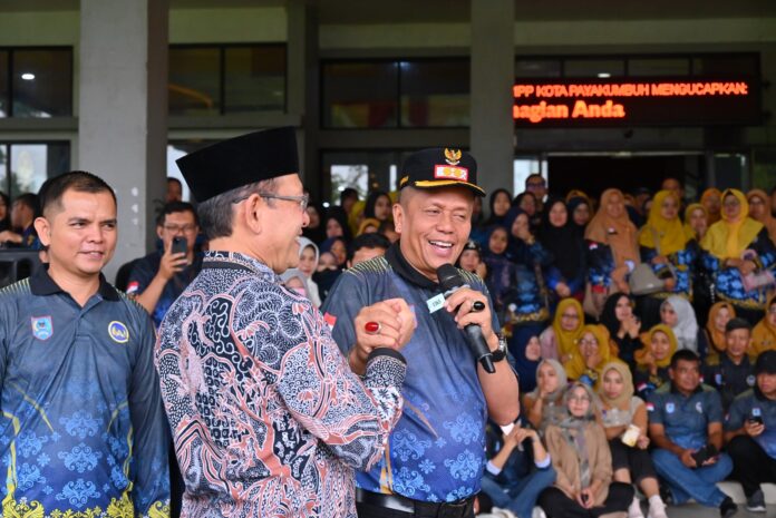 Soliditas Pimpinan Daerah: Wali Kota dan Wakil Wali Kota Meriahkan HUT KORPRI Payakumbuh Wali Kota Payakumbuh Zulmaeta berjabat tangan dengan Wakil Wali Kota Payakumbuh Elzadaswarman sambil berbicara menggunakan mikrofon pada peringatan HUT ke-54 KORPRI, di hadapan ASN yang memadati area acara.