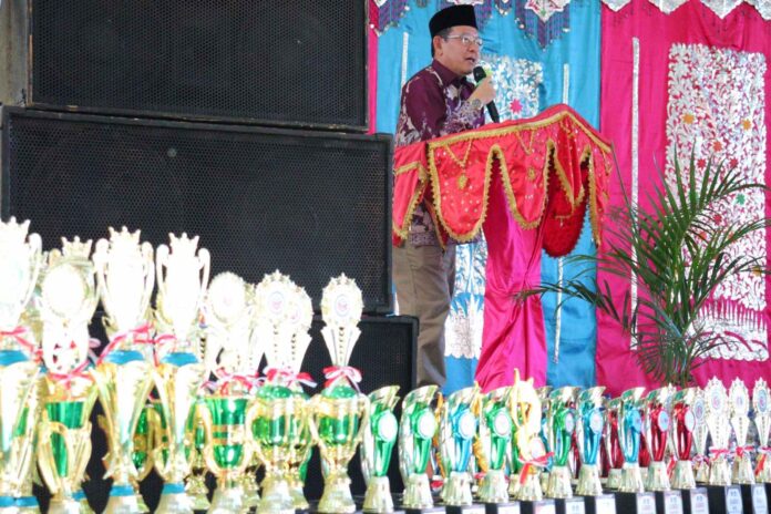 Wali Kota Payakumbuh menyampaikan sambutan pada Anugerah Prestasi Pendidikan 2025 dengan deretan piala penghargaan di depan panggung.